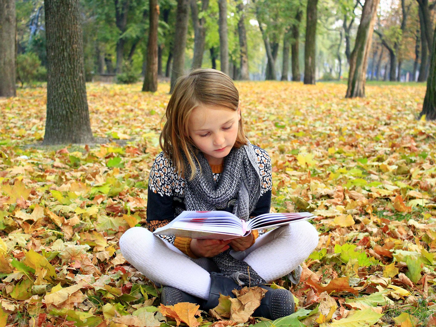 Child reading a book outdoors among autumn leaves
